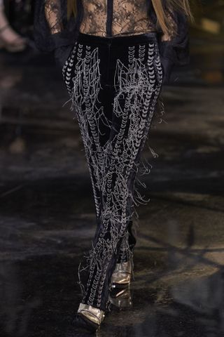A model walks the runway in highly unique trousers that a re covered in loose threads.