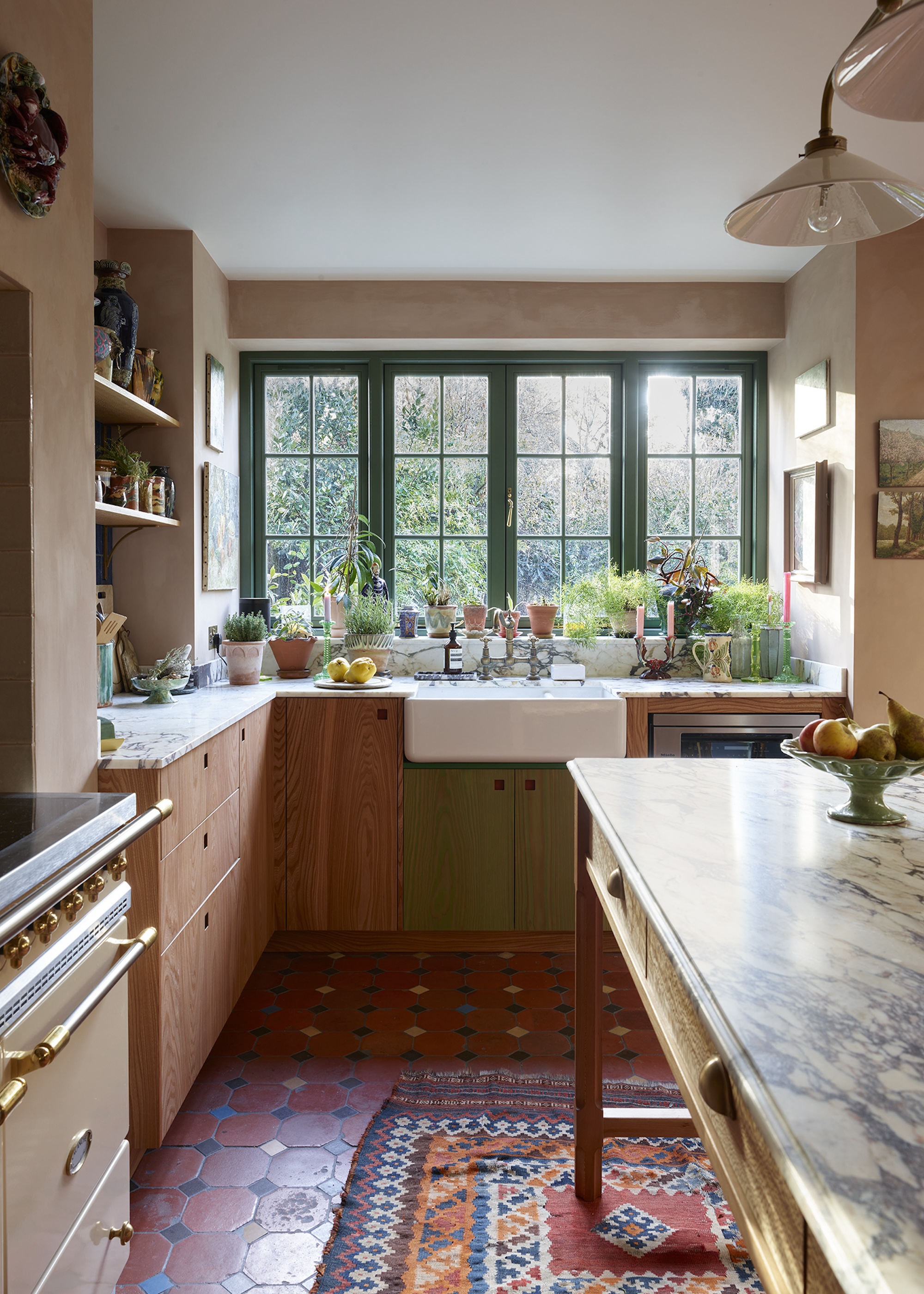 A flat fronted timber kitchen with cut-outs for handles shown with a vintage table for an island unit, terracotta tiled flooring and a traditional range cooker
