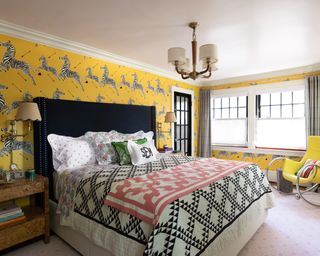 Bedroom with yellow zebra wallpaper, yellow armchair, black headboard, colorful, patterned pillows and throws