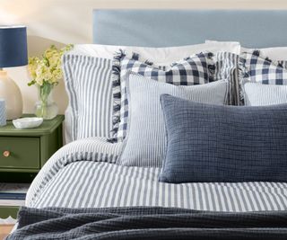 close up of bed with striped blue and white bedlined with checquered and plain cushions