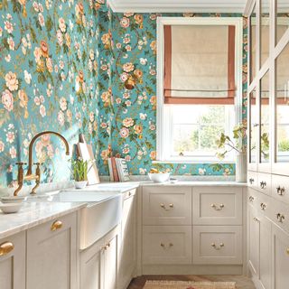 galley kitchen with green floral wallpaper and pattern blinds and white cabinetry sanderson