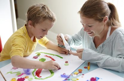Child, aged 6-7, and woman, aged 33, sticking buttons on a picture together in a family kitchen.