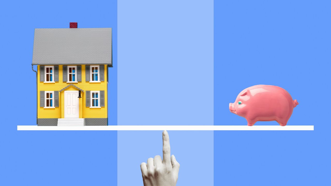 Yellow miniature model house and pink ceramic piggy bank on white line balanced on woman&#039;s finger