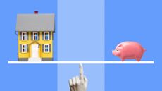 Yellow miniature model house and pink ceramic piggy bank on white line balanced on woman's finger