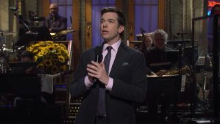 John Mulaney, wearing a suit, discusses his trip to rehab during SNL monologue.
