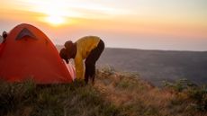 A man pitching his tent on the side of a hill