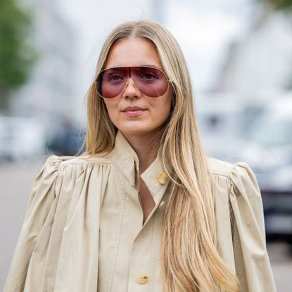 woman with tinted maroon sunglasses wearing a beige military style jacket with long, straight blonde hair - best hair straighteners