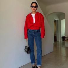 Aimee Song wears a red jacket, dark wash blue jeans, Chanel flats and purse and a pearl necklace.