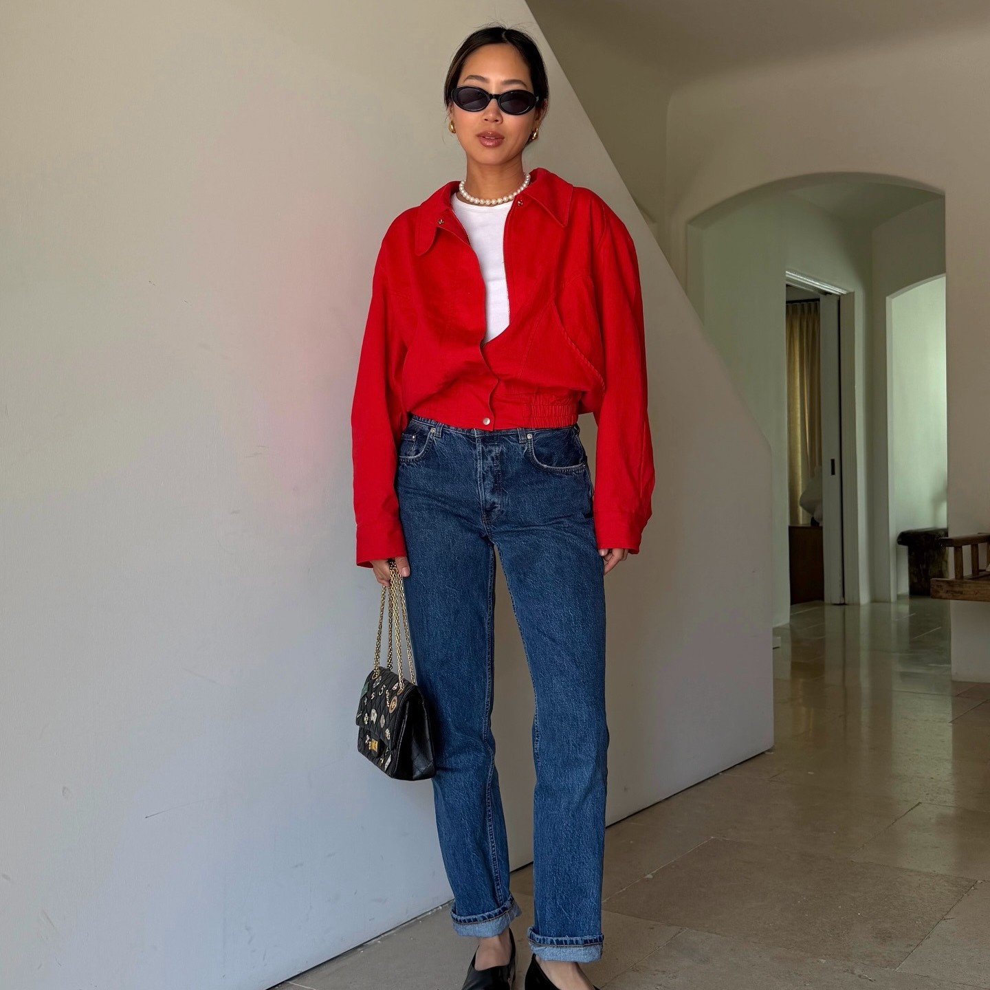 Aimee Song wears a red jacket, dark wash blue jeans, Chanel flats and purse and a pearl necklace.