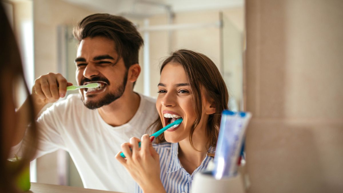 A couple brushing their teeth in front of a bathroom mirror