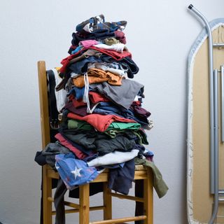 A pile of dirty clothes on a wooden chair with an iron in the background