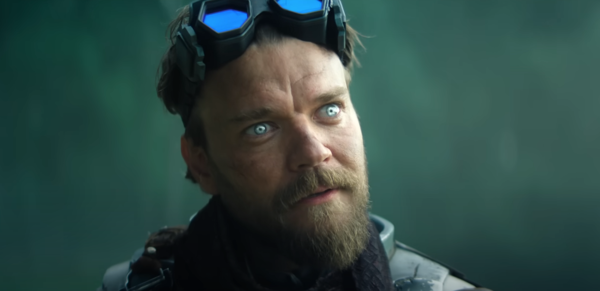 A sinister bearded man with scary eyes and wearing goggles