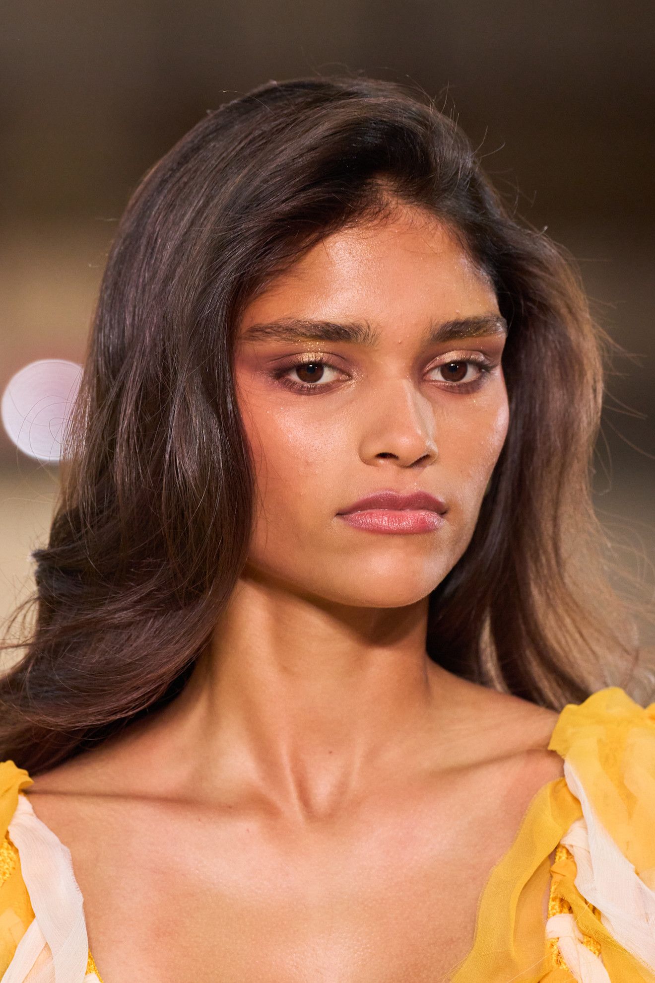 Lip gloss lids at Carolina Herrera on a model with brown hair in a yellow dress.