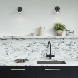 black kitchen spotlights above a white and grey marble effect worktop and black cabinets