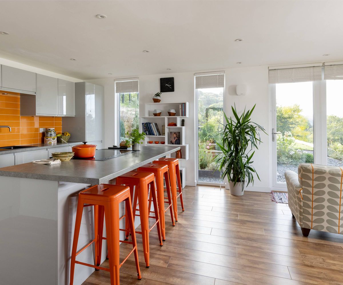 Kitchen and living area in an orange colour scheme with four bar stools and kitchen island and full height windows