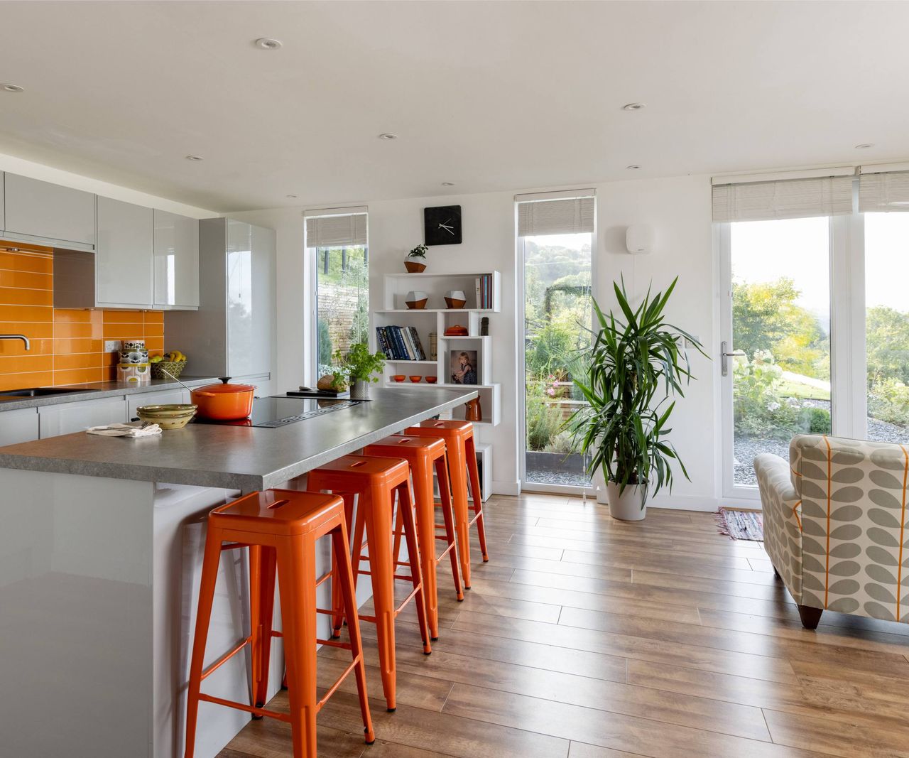 Kitchen and living area in an orange colour scheme with four bar stools and kitchen island and full height windows