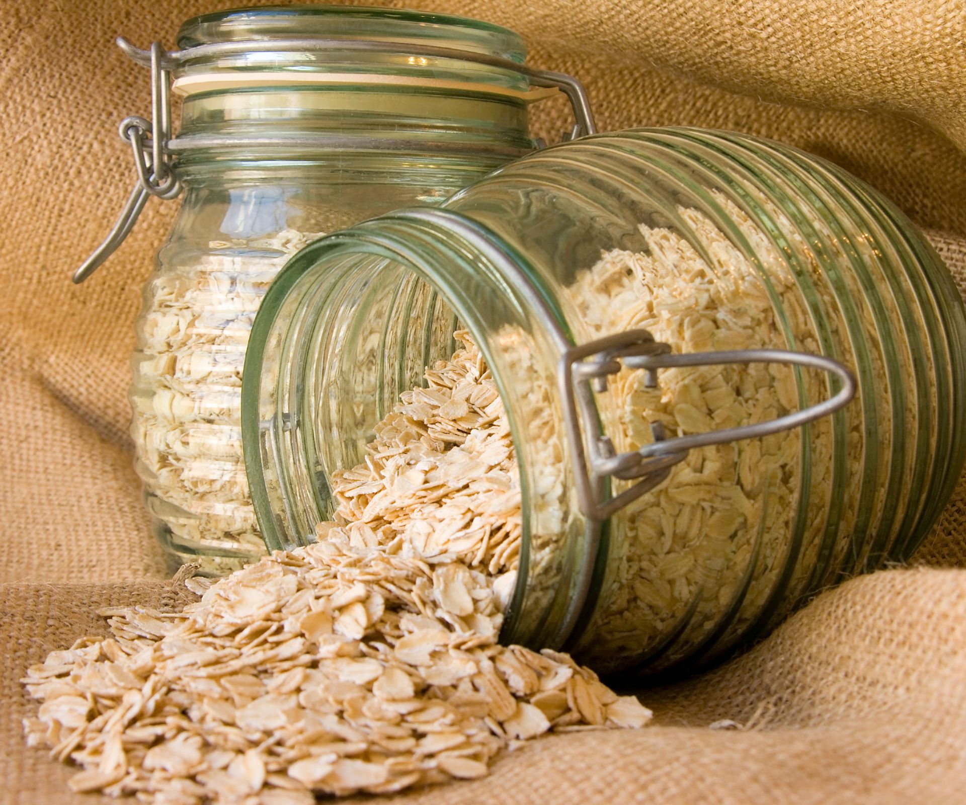 plain rolled oats spilling out of a glass storage jar on hessian fabric