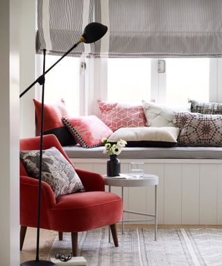 Window seat with Roman blind above and pillows and orange armchair