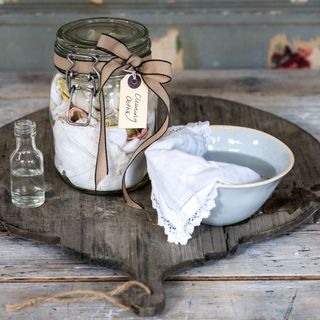 bowl and cloth glass jar with ribbon and cleaning liquid on wooden board