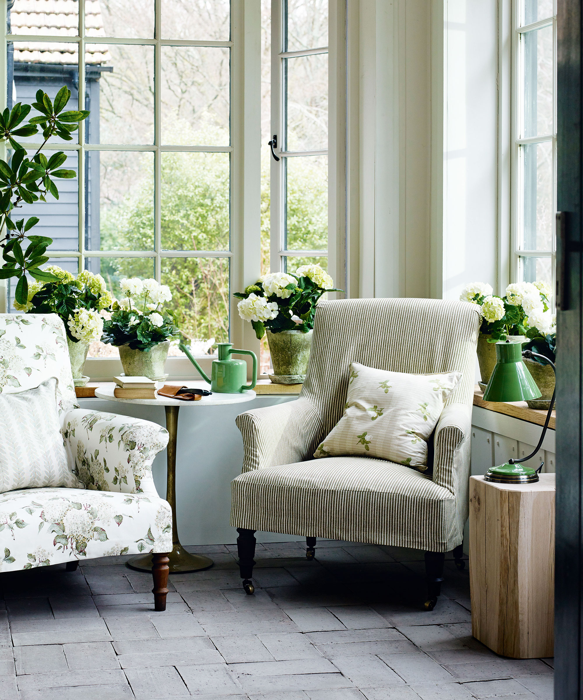 Garden room ideas with country style decor, two armchairs, stone flooring, plants and flowers on windowsill