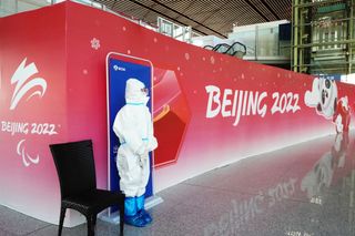 An image of a health worker standing in front of a Beijing 2022 sign
