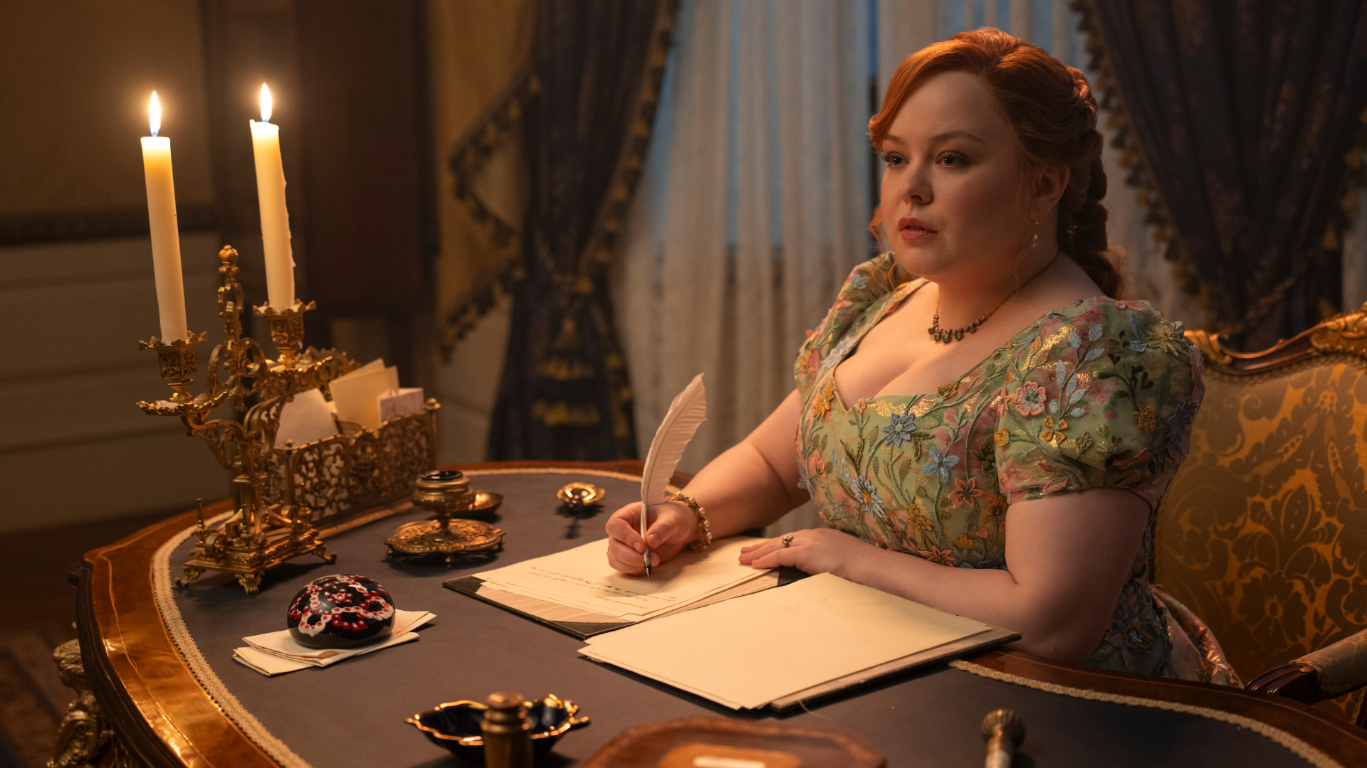 A woman (Nicola Coughlan as Penelope Bridgerton) writes with a feather quill at a Regency-era drawing table, in episode 405 of Bridgerton.