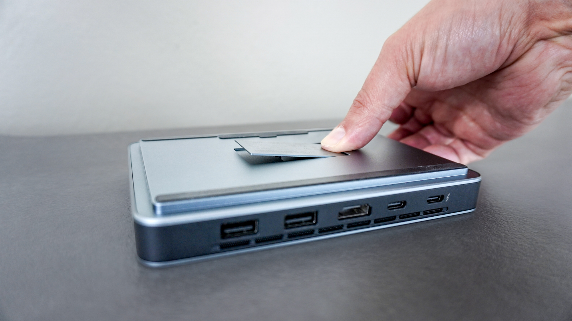 A person pressing on the magnetic cover on the bottom of the Khadas Mind 2S to reveal its free M.2 SSD slot