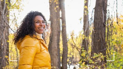 Woman smiling over her shoulder, soft hiking in bright jacket through the forest