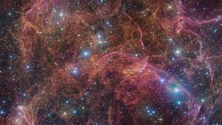 This image shows a spectacular view of the orange and pink clouds that make up what remains after the explosive death of a massive star — the Vela supernova remnant.