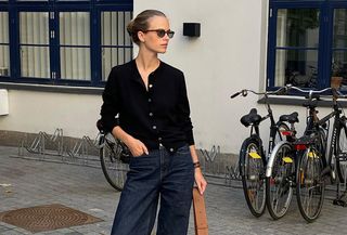 Woman wearing a black cardigan, dark-wash jeans, and sunglasses.