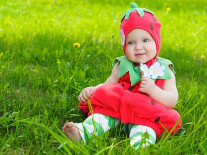 Baby In DIY Strawberry Plant Costum Sitting On Green Grass