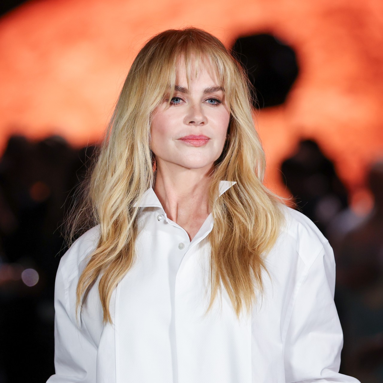 a white woman with long blonde hair and bangs posing for paparazzi at a fashion show