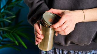 Taking the lid off the Wacaco Pipamoka portable coffee maker in front of a blue background.