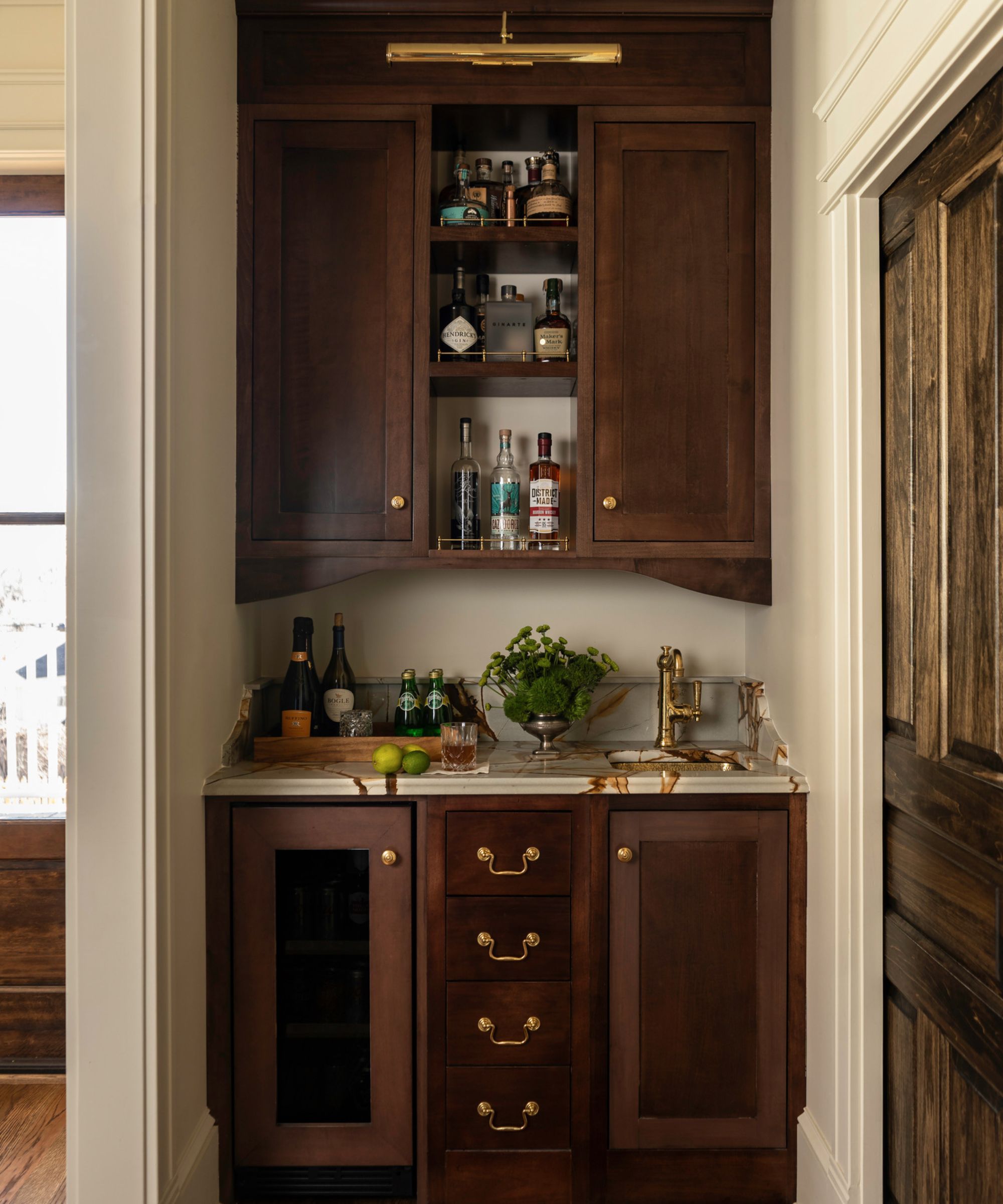 A small home bar area with wooden cabinets and marble countertops with a sidesplash