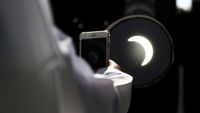 A man takes a picture on his mobile phone of the partial solar eclipse.