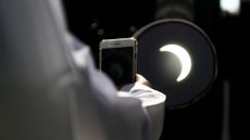 A man takes a picture on his mobile phone of the partial solar eclipse.
