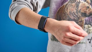 the amazfit helio strap fitness tracker with a screenless design, showing the gray strap worn around the wrist and the charger