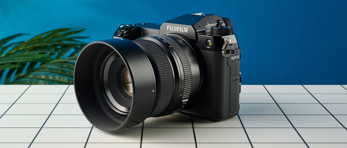 The Fujifilm GFX100S II on a white surface with a blue wall in the background