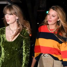 Taylor Swift wears a green velvet dress and walks with Blake Lively, who is wearing a red and orange sweater