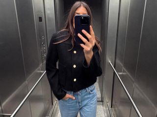 Influencer Maja Weyhe posing for an elevator selfie wearing a round neck cropped black jacket with gold buttons paired with jeans