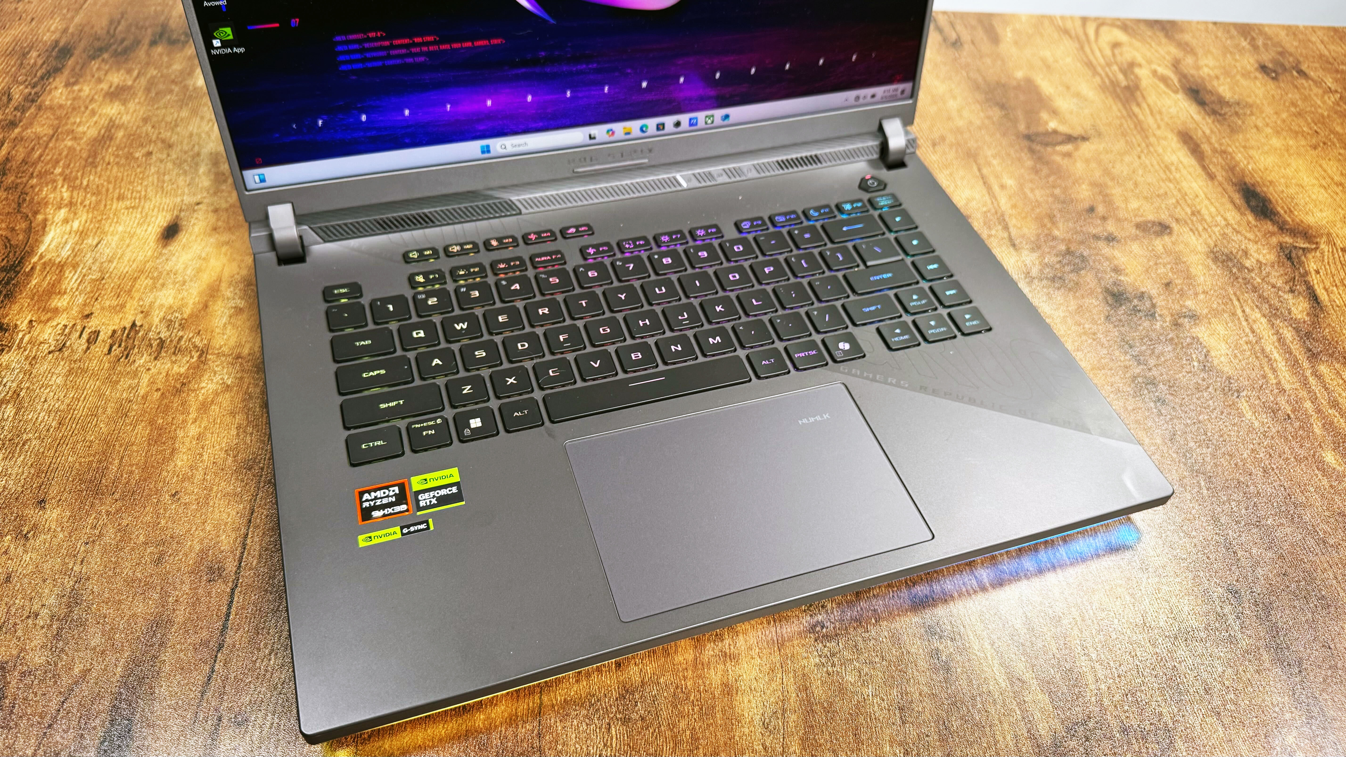 Top-angle shot of the Asus ROG Strix G16 (G614FR) gaming laptop's keyboard on a wooden desk against a gray background.
