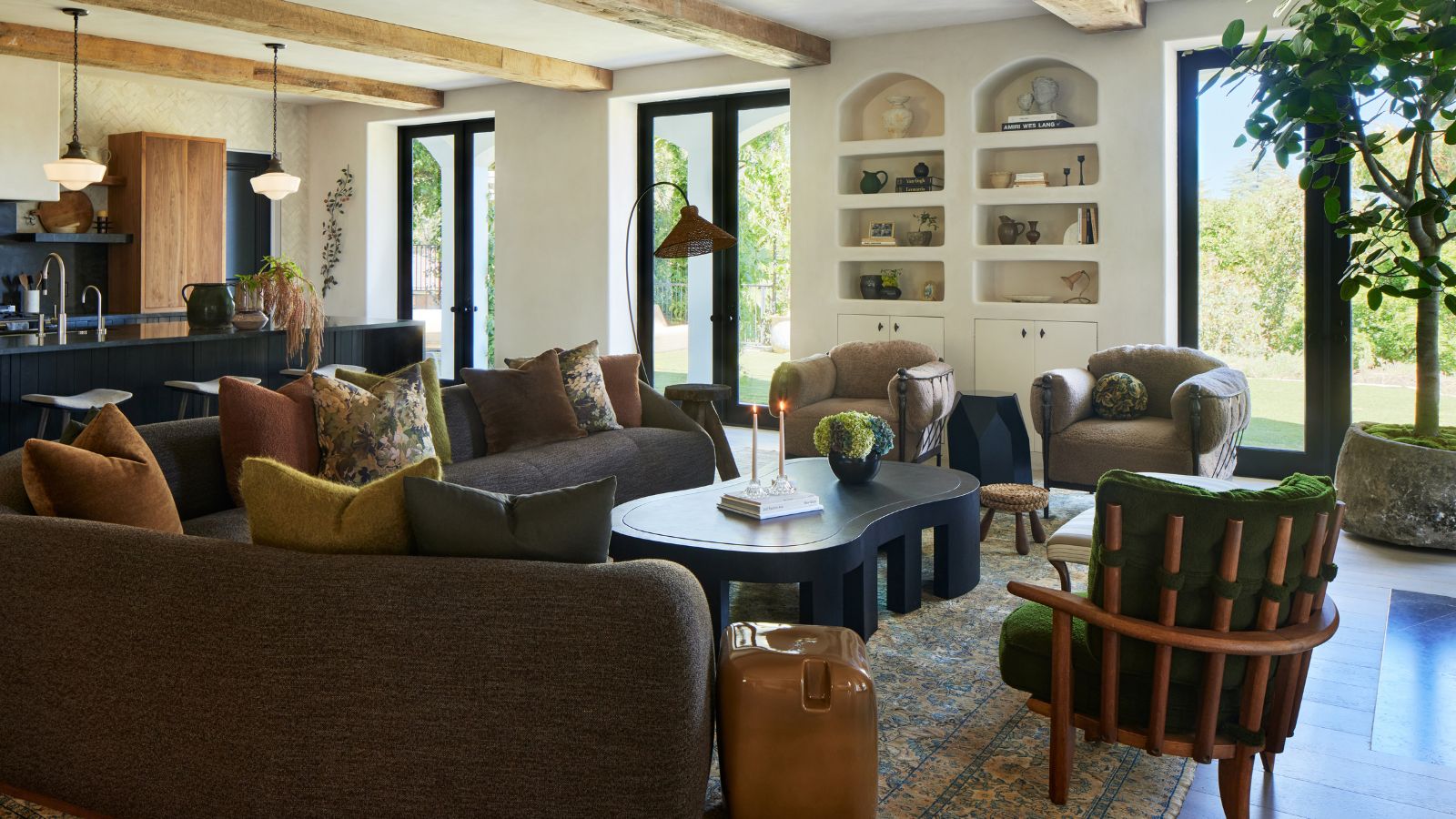 Living room with built-in alcove shelving, brown sectional with colourful pillows, abstract modern coffee table, green midcentury armchair and two beige armchairs and neutral floral carpet