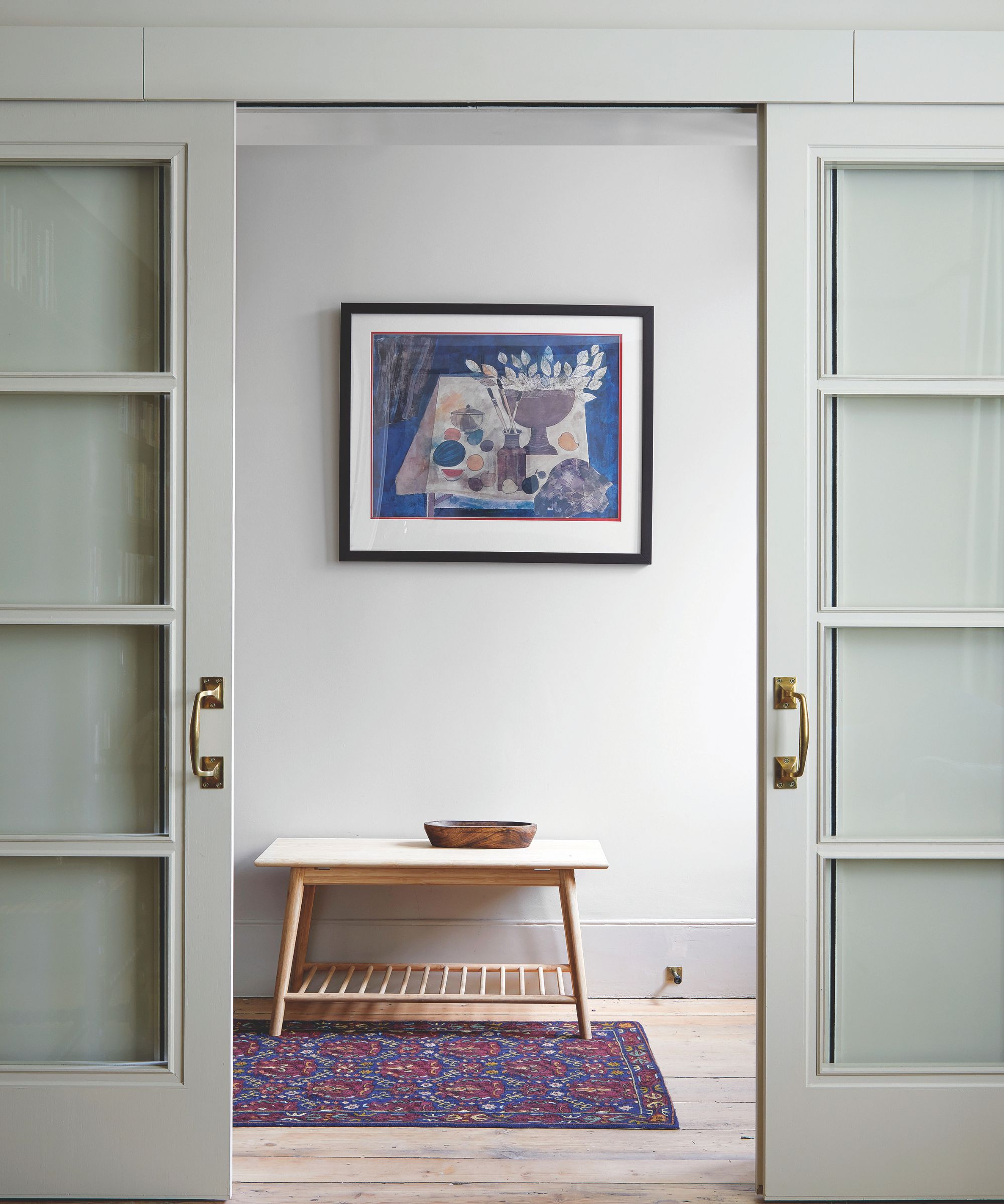 Minimal hallway with modern art on wall, sliding doors, wooden console and red and blue persian rug