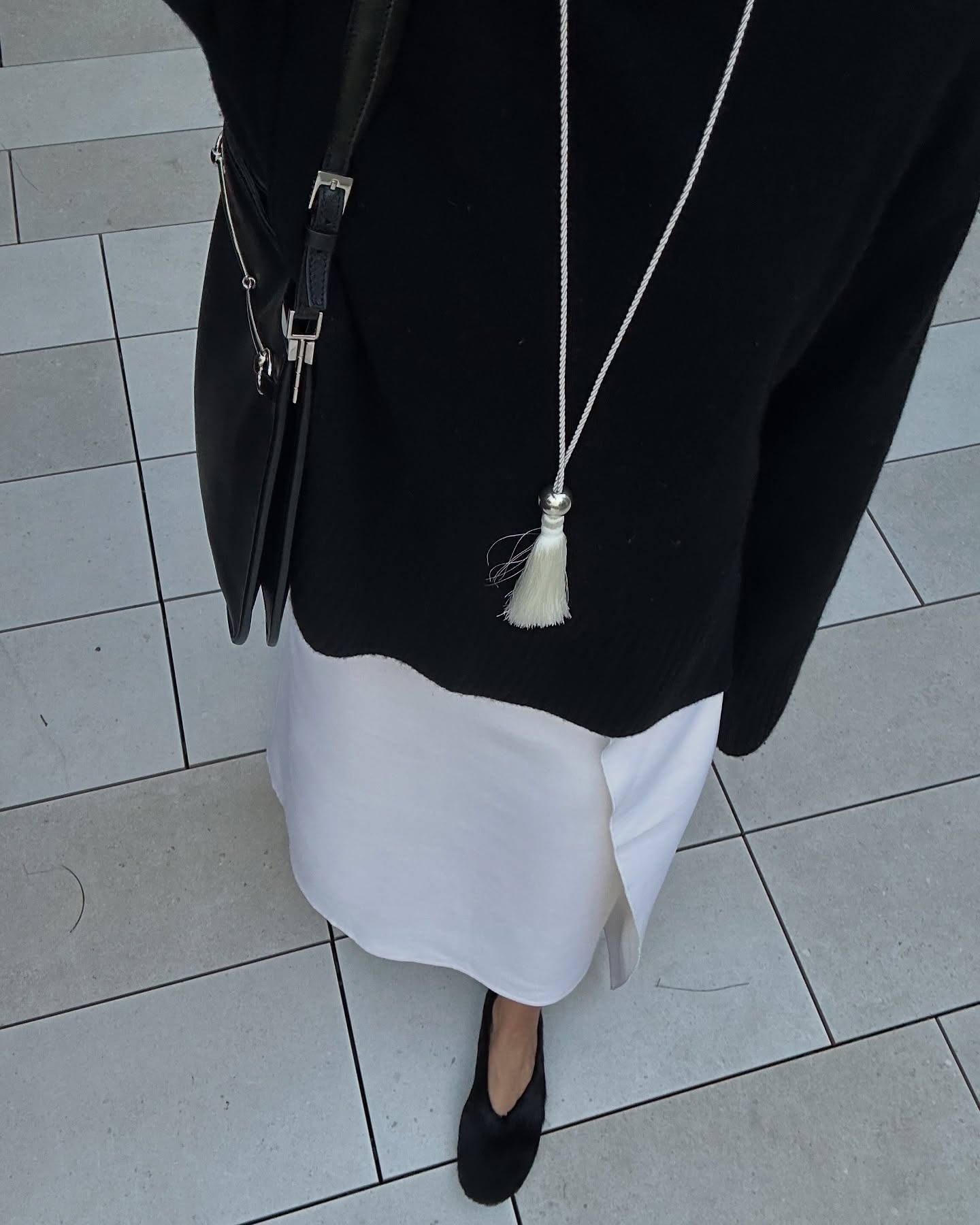 Debora Brosa wearing a black top, cream necklace, and white skirt.
