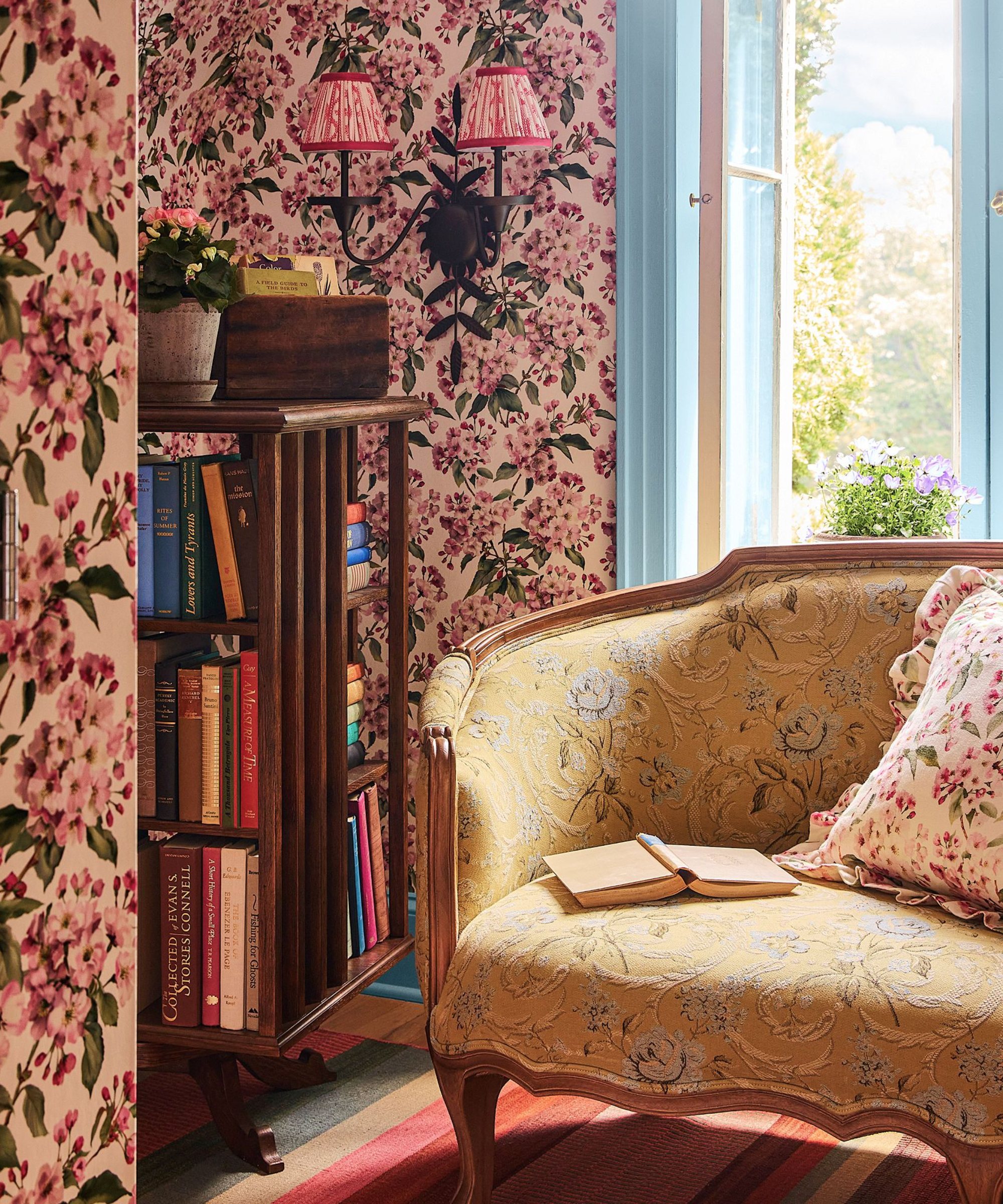 a small book nook with a vintage armchair, a small bookshelf with many books, and a sconce on the wall