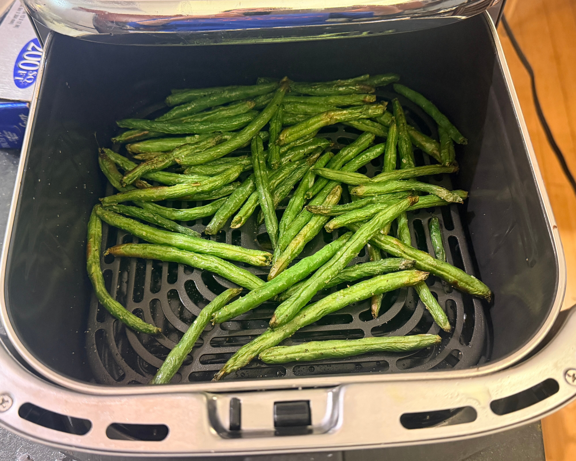Green beans in an air fryer basket, sitting on a gray countertop