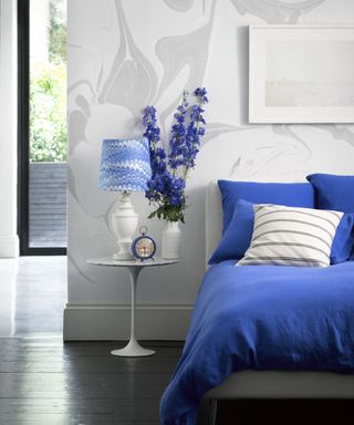 White bedroom with marble wallpaper, blue duvet and feathered detailed lampshade