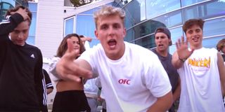 Jake Paul singing in front of a huge house with a white t-shirt on.