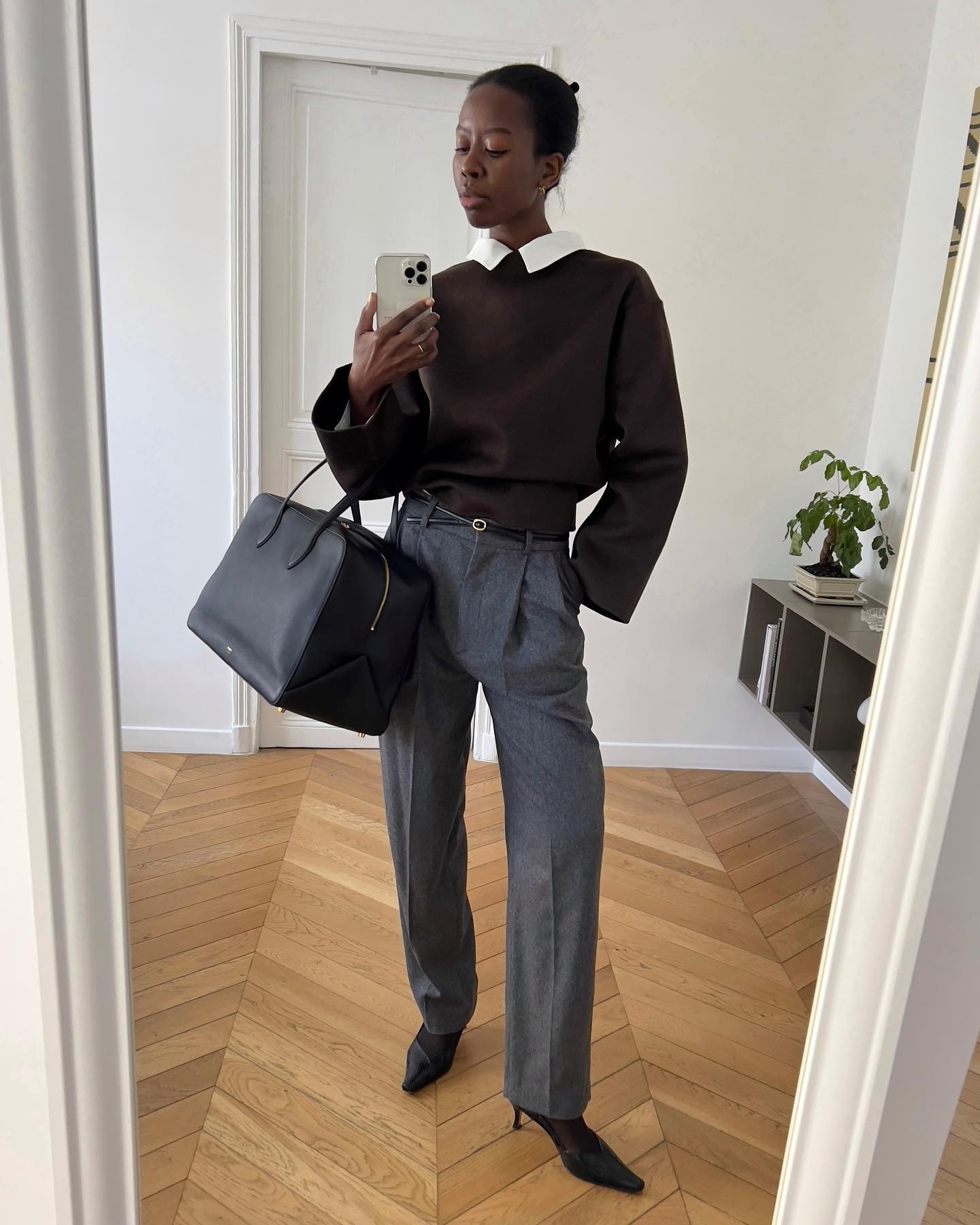 Sylvie Mus holding a structured black duffle bag against tailored gray pants.