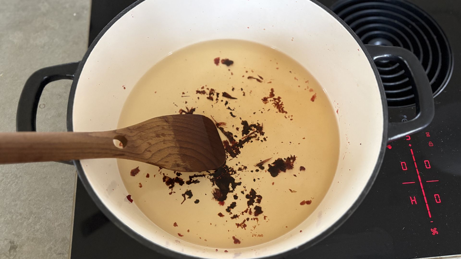 A stage of cleaning a burnt cast iron casserole dish on a hob